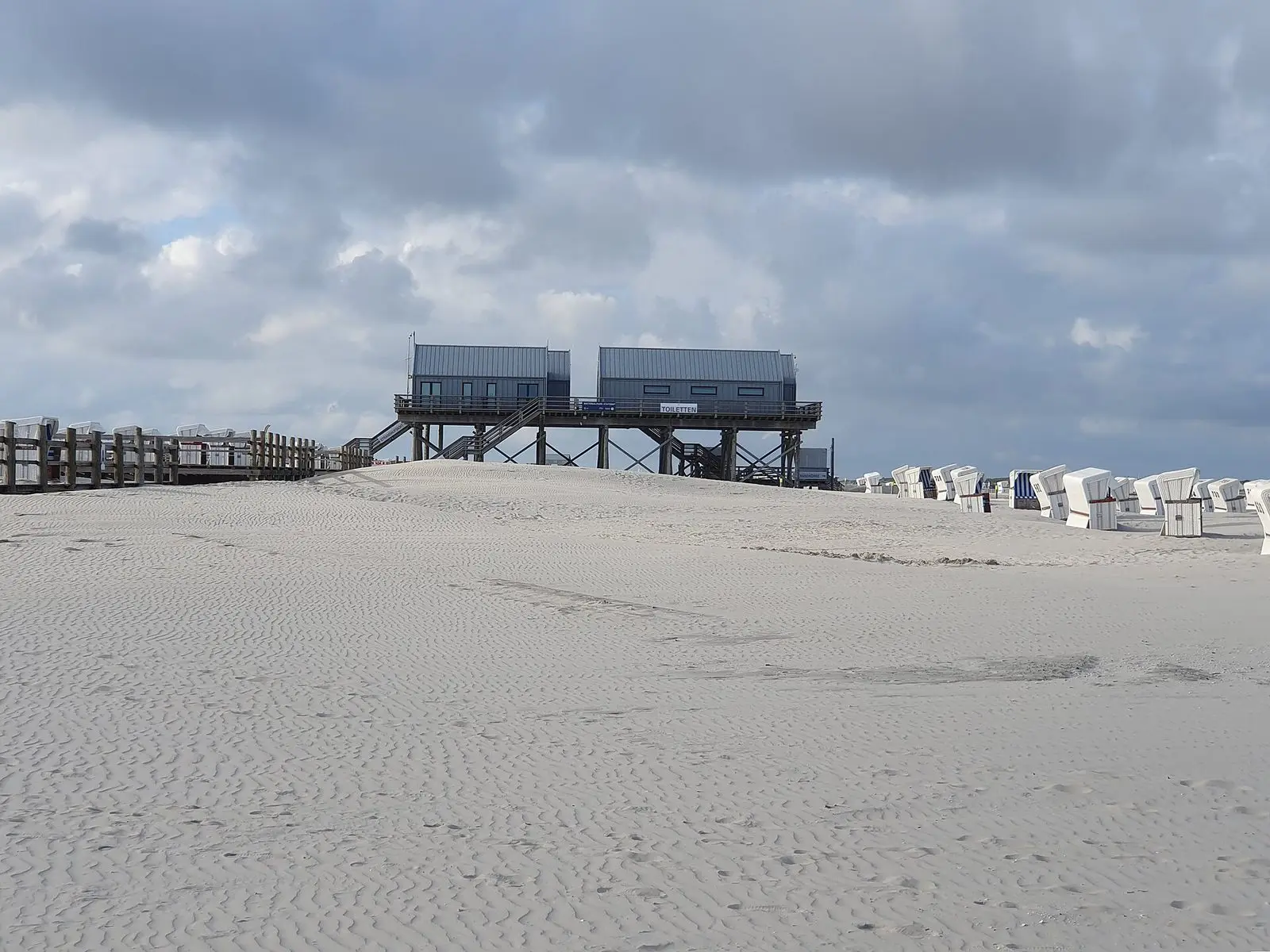 Weiter, flacher Sandstrand in Ording mit dem Pfahlbau der Strandaufsicht, Holzsteg und Strandkörben