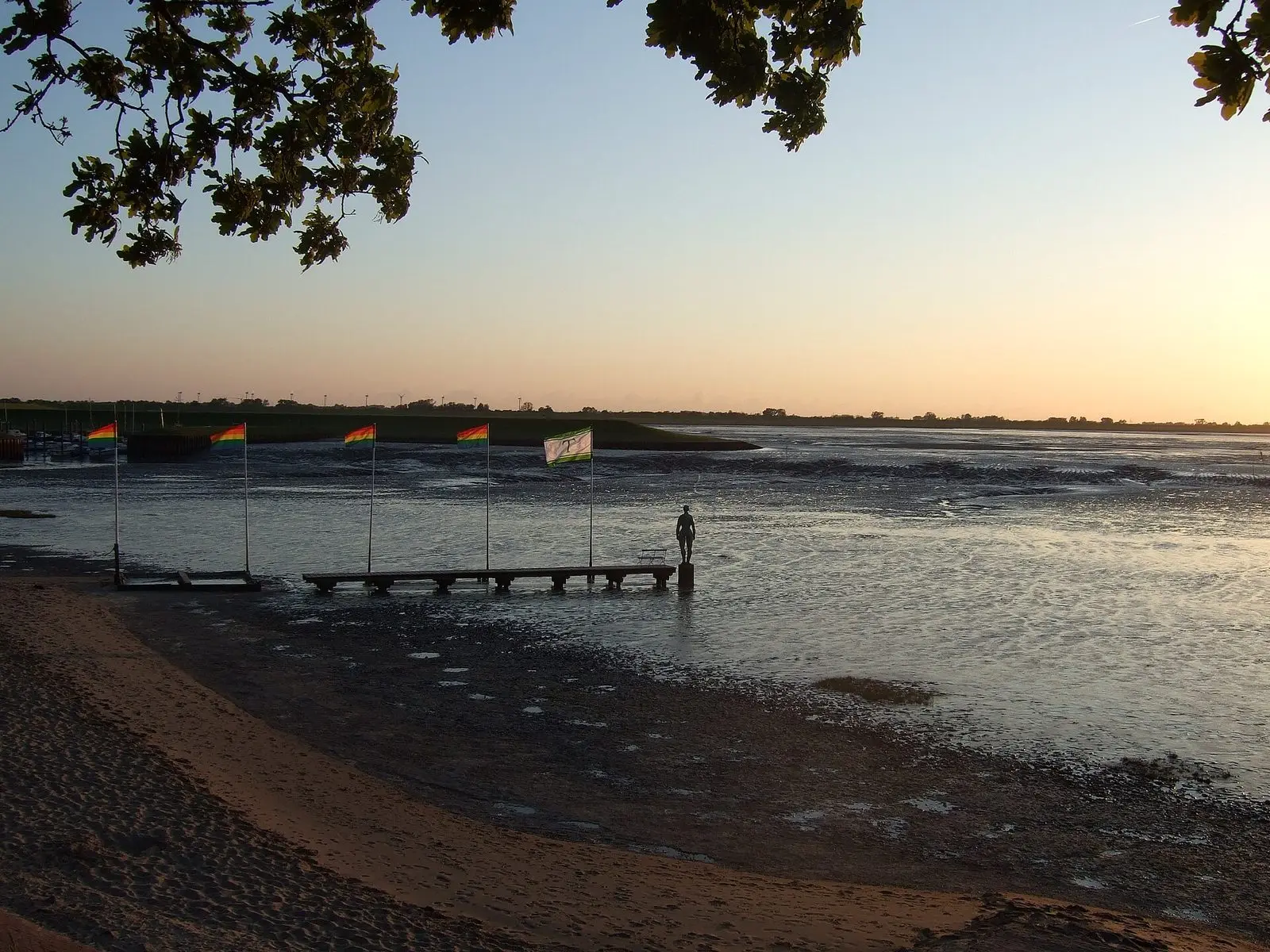 Abendstimmung am Dangaster Strand mit Flaggen und der Skulptur ‚Jade‘ im Watt