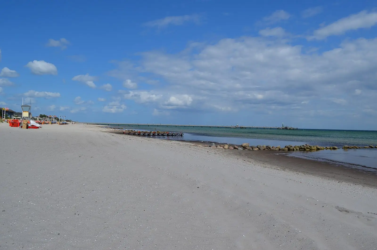 Weiter, fast leerer Sandstrand von Grömitz mit Buhnen und Seebrücke am Horizont